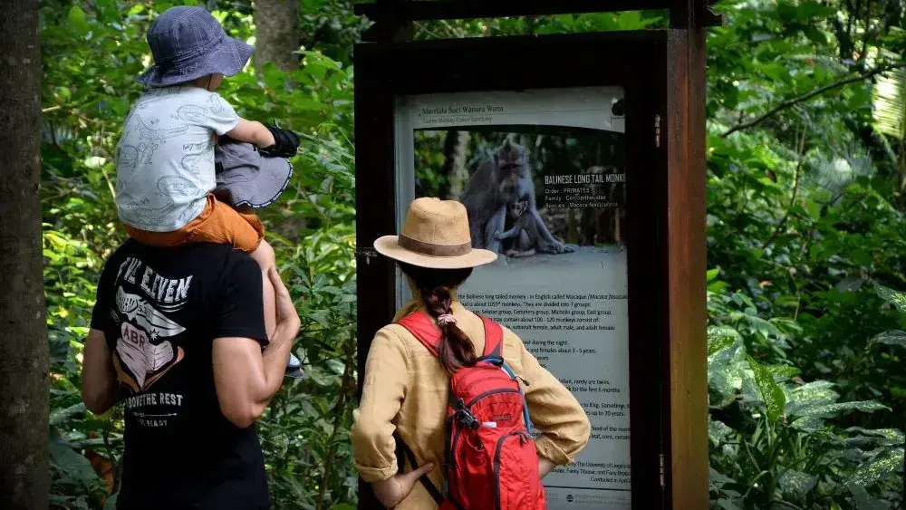 Parents with a child on shoulders reading a sign in the Ubud Monkey Forest jungle