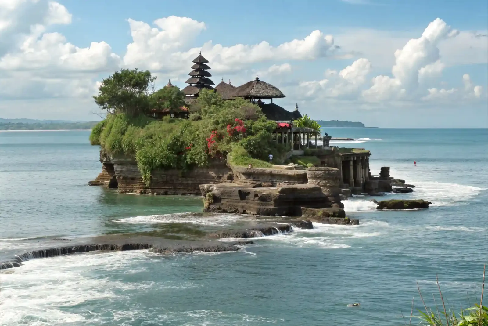 Tanah Lot sea temple on its rocky outcrop surrounded by surf and blue sky, Bali