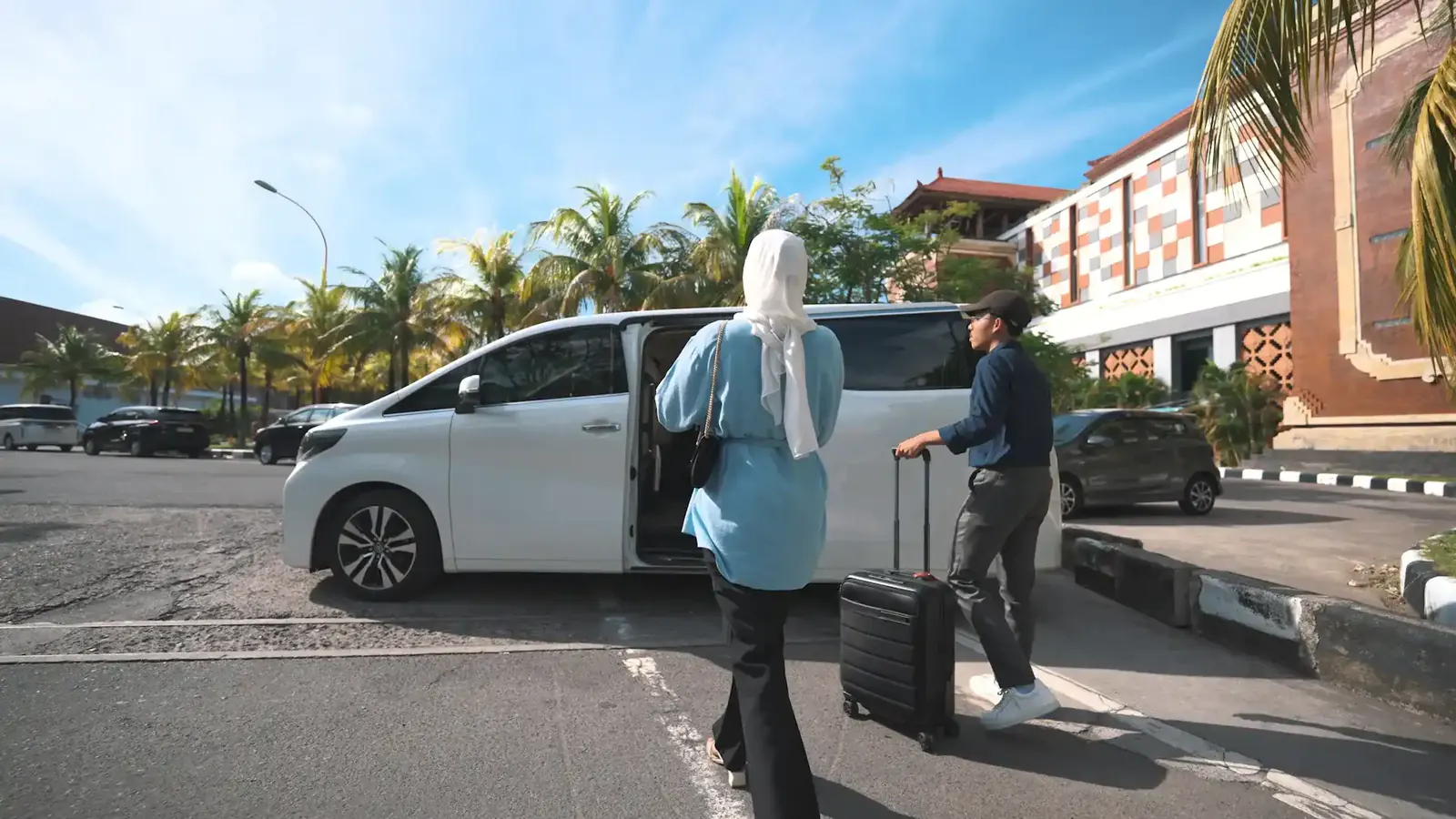 Driver loading luggage into a white Toyota Alphard for guests at Bali's Ngurah Rai airport