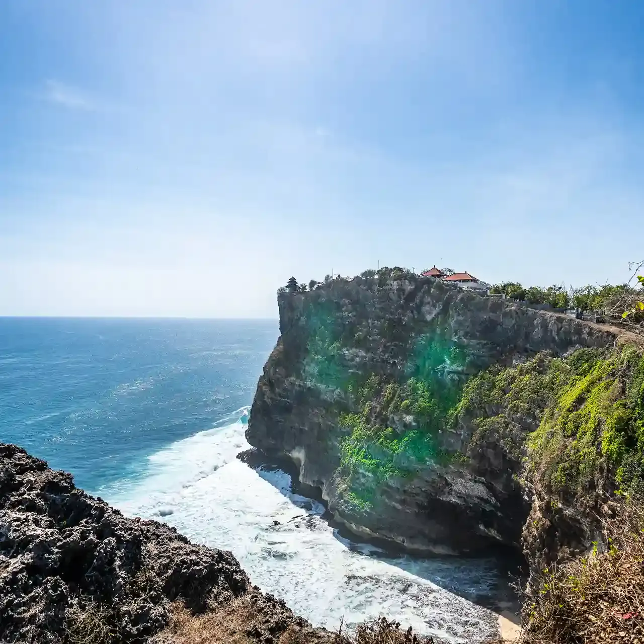 Sheer limestone cliff at Uluwatu with Pura Luhur Uluwatu temple on top above crashing surf