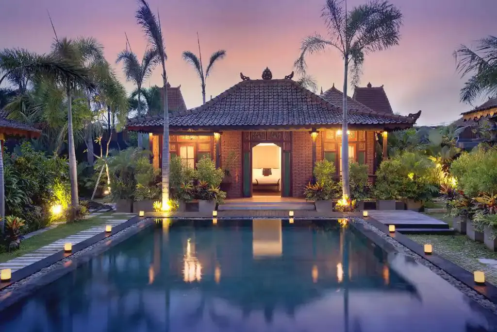 Balinese-Javanese style villa pavilion lit at dusk behind a candle-lined private pool in Bali